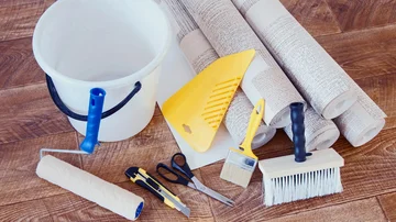 Verschiedenen Werkzeuge zum tapezieren, Pinsel, Rollen, Cutter, Schere, Eimer und Tapeten.